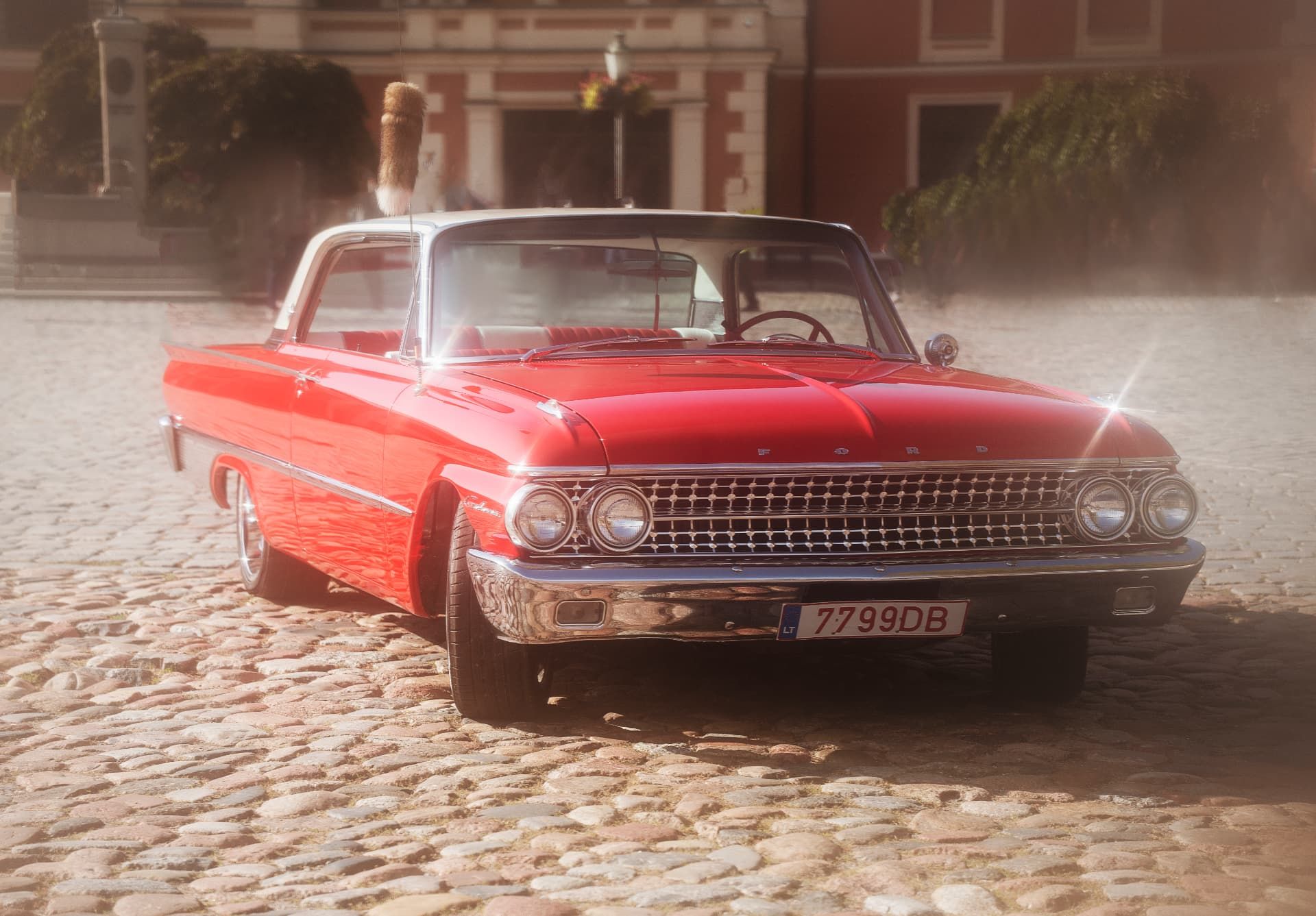 Raudonas 1961 m. Ford Galaxie su baltu stogu, priekis su chromuotomis grotelėmis, grįstoje senamiesčio aikštėje
